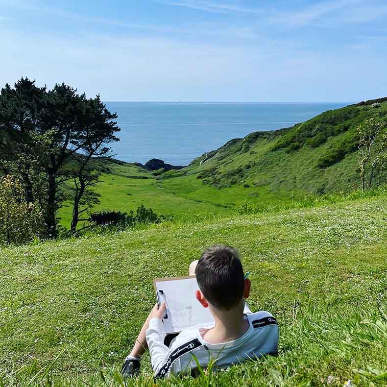 Boy on the grass with a clip board overlooking the sea